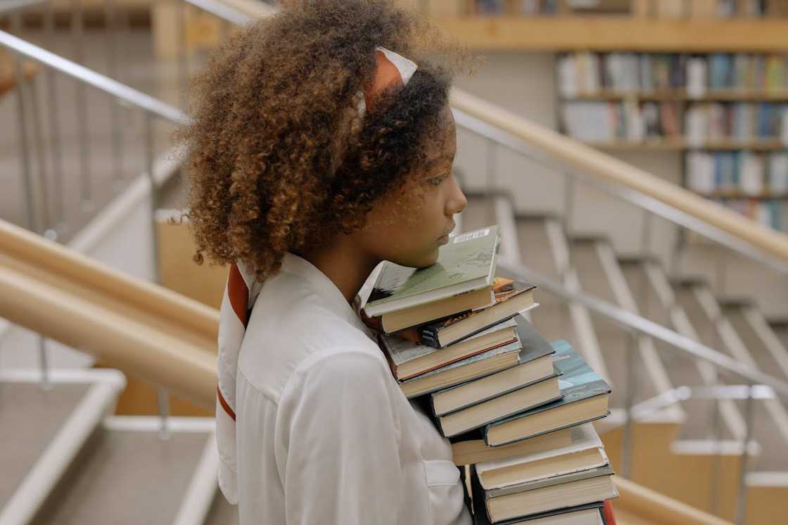 A young woman carrying a tall stack of books.