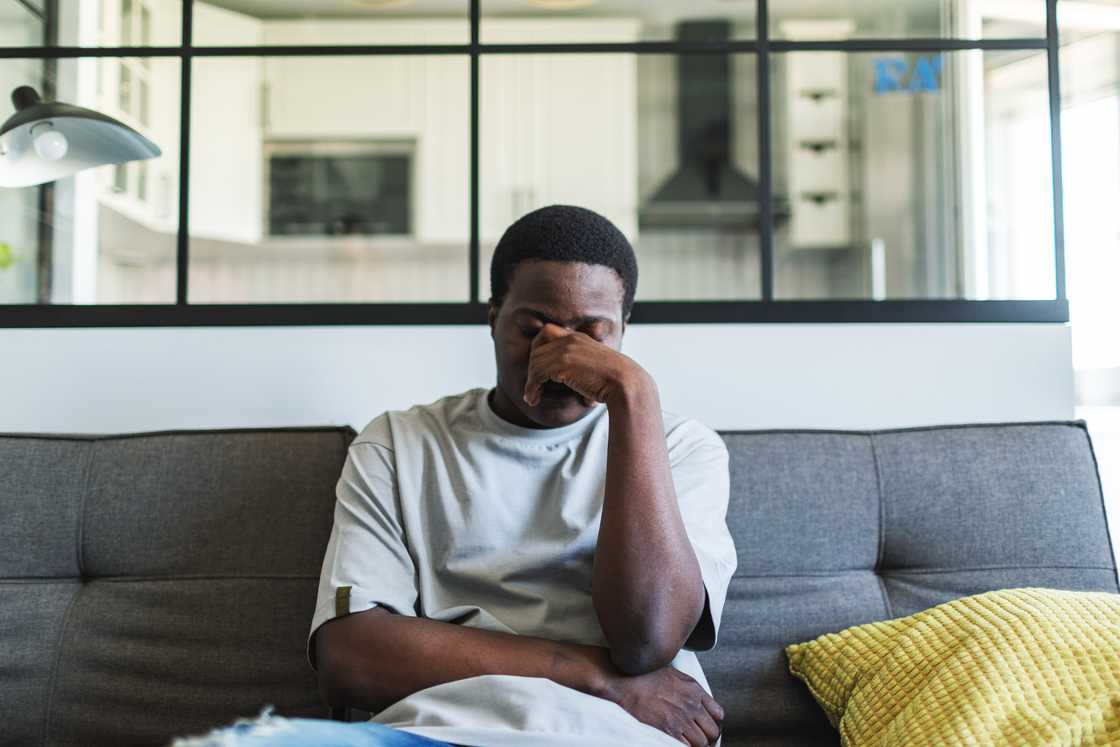 Person crying in soft morning light, sitting upright on sofa.