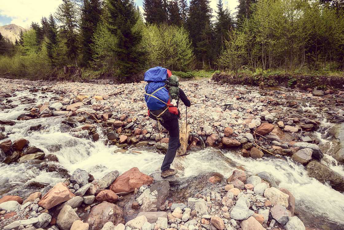 A traveller with a backpack crosses a mountain river. A traveller with a backpack crosses a mountain river.