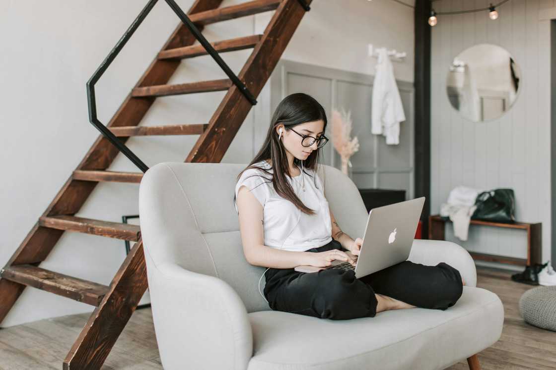 A woman is seated on a grey coach holding a laptop