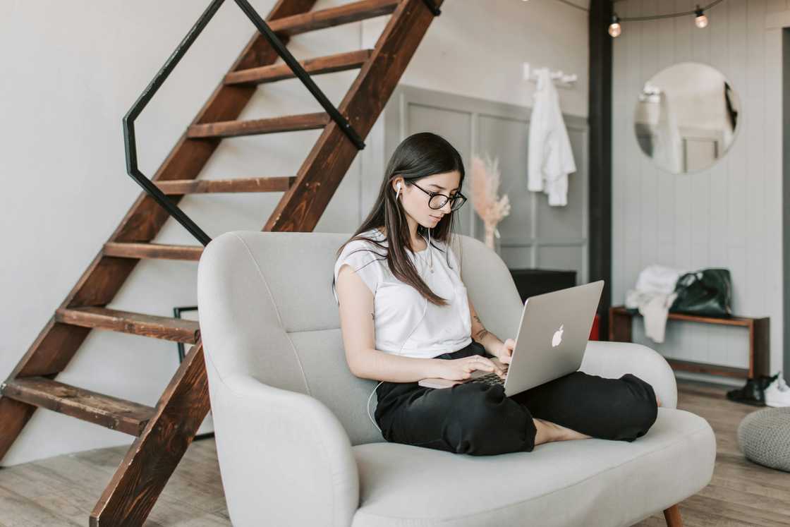 A woman is seated on a grey coach holding a laptop A woman is seated on a grey coach holding a laptop