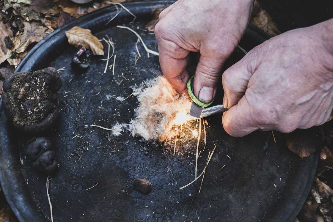 A person uses friction to start a campfire.