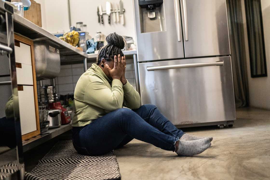 A woman sits sobbing on the kitchen floor.