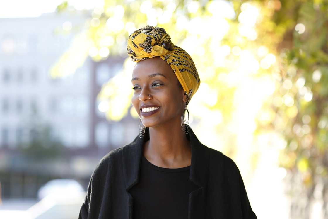 Beautiful, young, happy Muslim woman photographed in a bright outdoor urban setting wearing a yellow, decorated wrap around her head. Beautiful, young, happy Muslim woman photographed in a bright outdoor urban setting wearing a yellow, decorated wrap around her head.