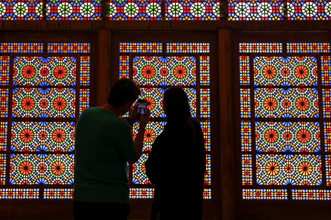 A man and a woman stand in front a stained glass window at Dowlat Abad Garden in Iran's central city of Yazd on July 3, 2023 A man and a woman stand in front a stained glass window at Dowlat Abad Garden in Iran's central city of Yazd on July 3, 2023