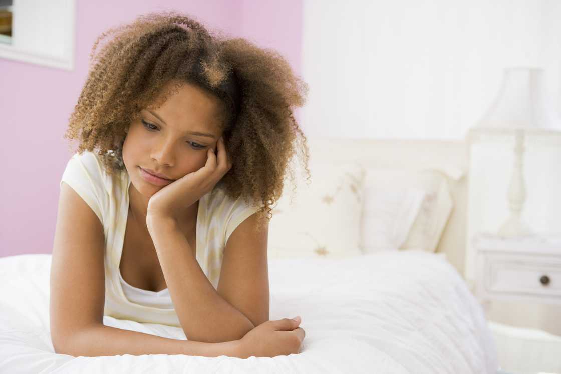 Young person lies on a white bed, resting their head on one hand in a thoughtful pose. Young person lies on a white bed, resting their head on one hand in a thoughtful pose.