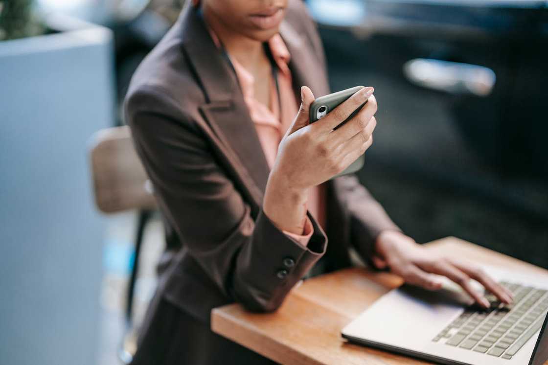 A woman sits at a desk using a phone beside an open laptop. A woman sits at a desk using a phone beside an open laptop.