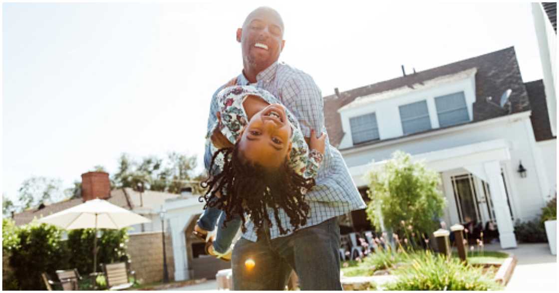 A father plays with his daughter in front of their house