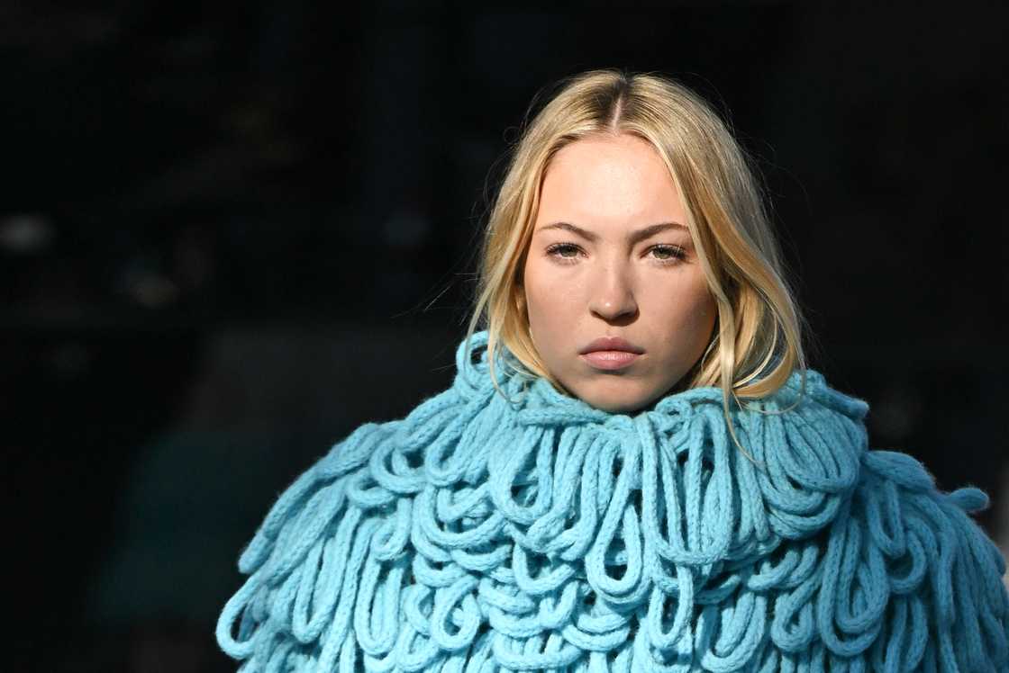 Lila Moss in blue is posing against a dark background in Paris, France