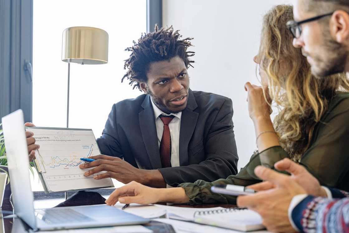 A man in a suit points at a document while speaking to two people.