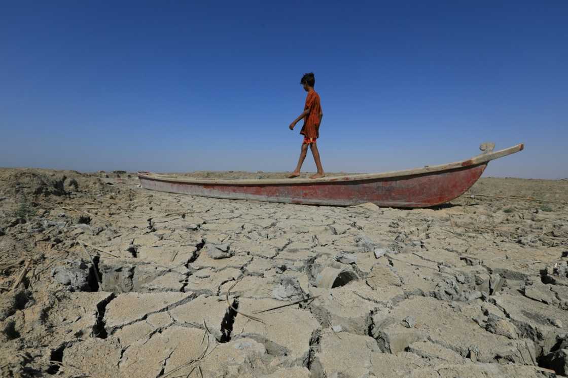 A boy walks on a boat on the dried-up bed of a section of Iraq's receding southern marshes of Chibayish in Dhi Qar province amid a drought seen as worsened by climate change A boy walks on a boat on the dried-up bed of a section of Iraq's receding southern marshes of Chibayish in Dhi Qar province amid a drought seen as worsened by climate change
