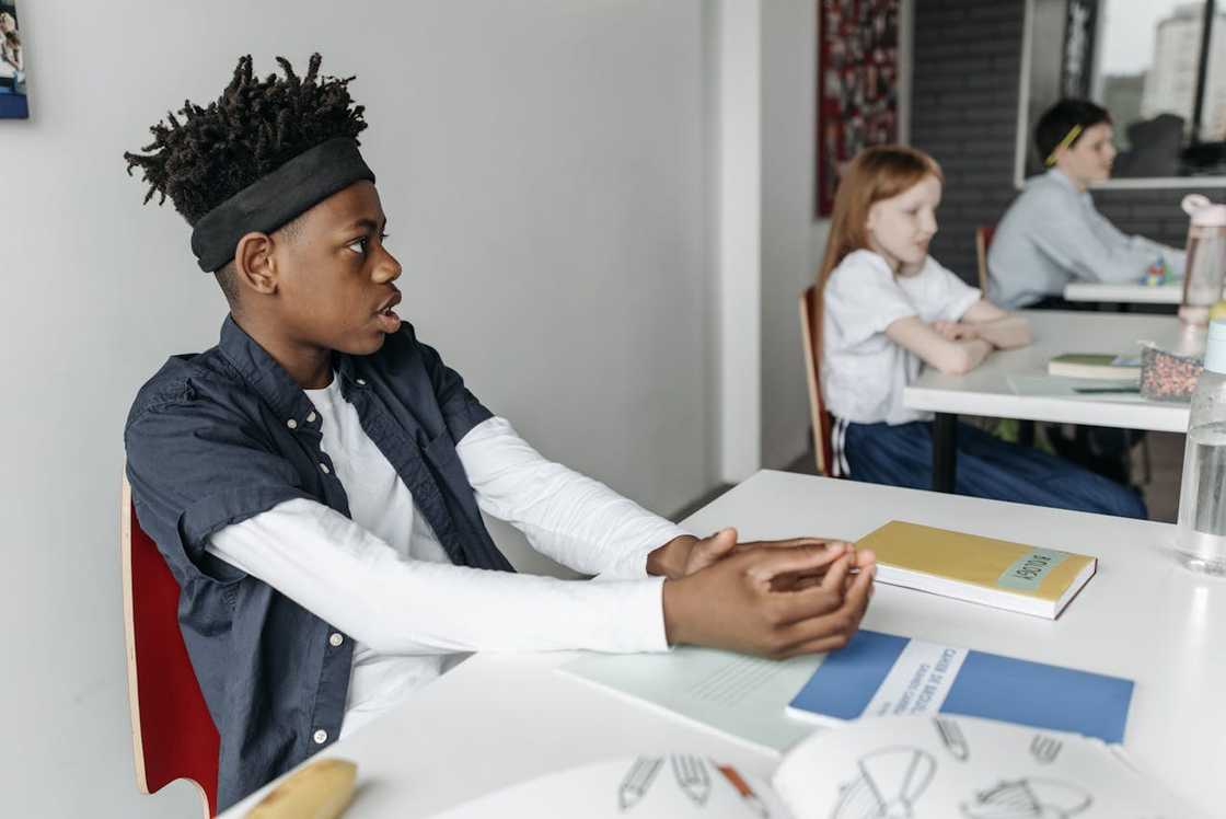 A student sits at a desk while classmates work behind him.