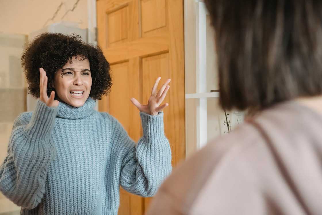 A woman gestures angrily while speaking to another woman inside a home.