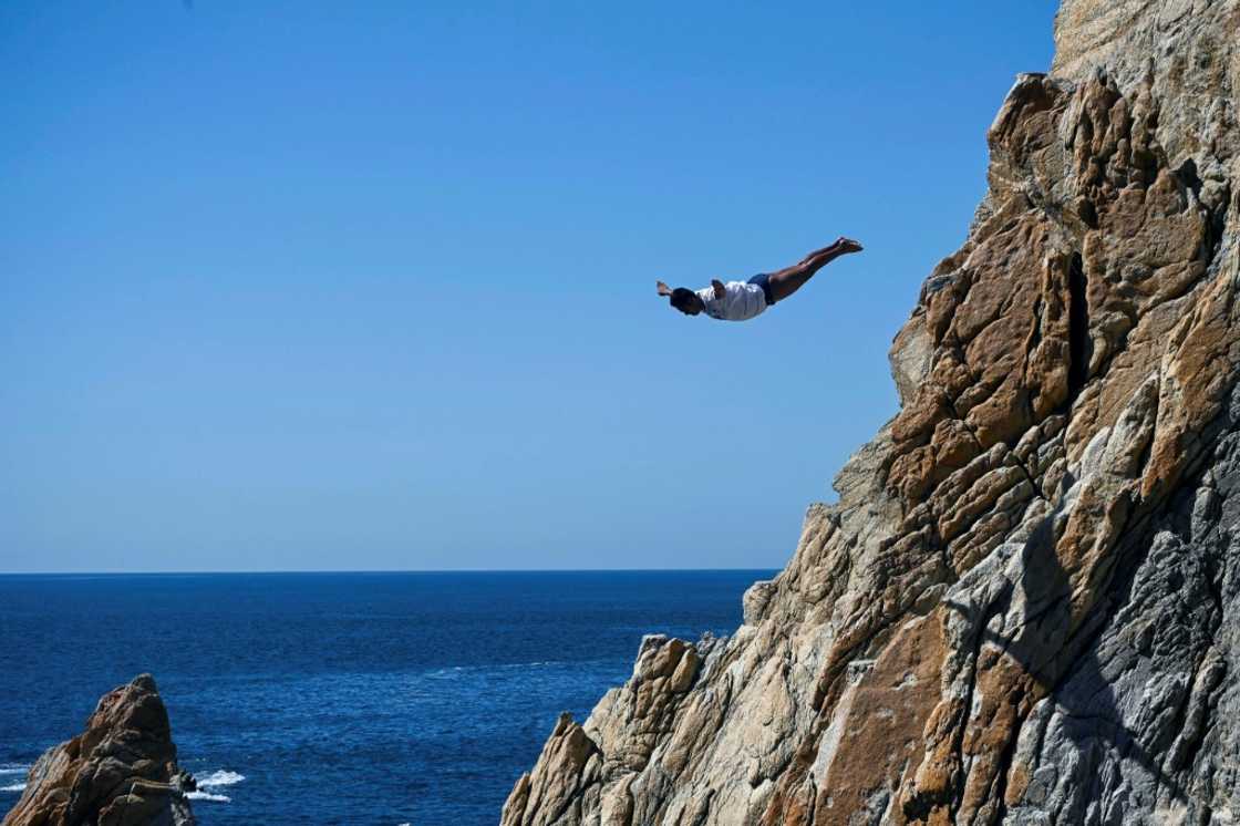 A cliff diver leaps from the rocks above Acapulco after the Mexican resort allowed resumption of the  activity in the aftermath of deadly Hurricane Otis, but tourists are only slowly returning to the region