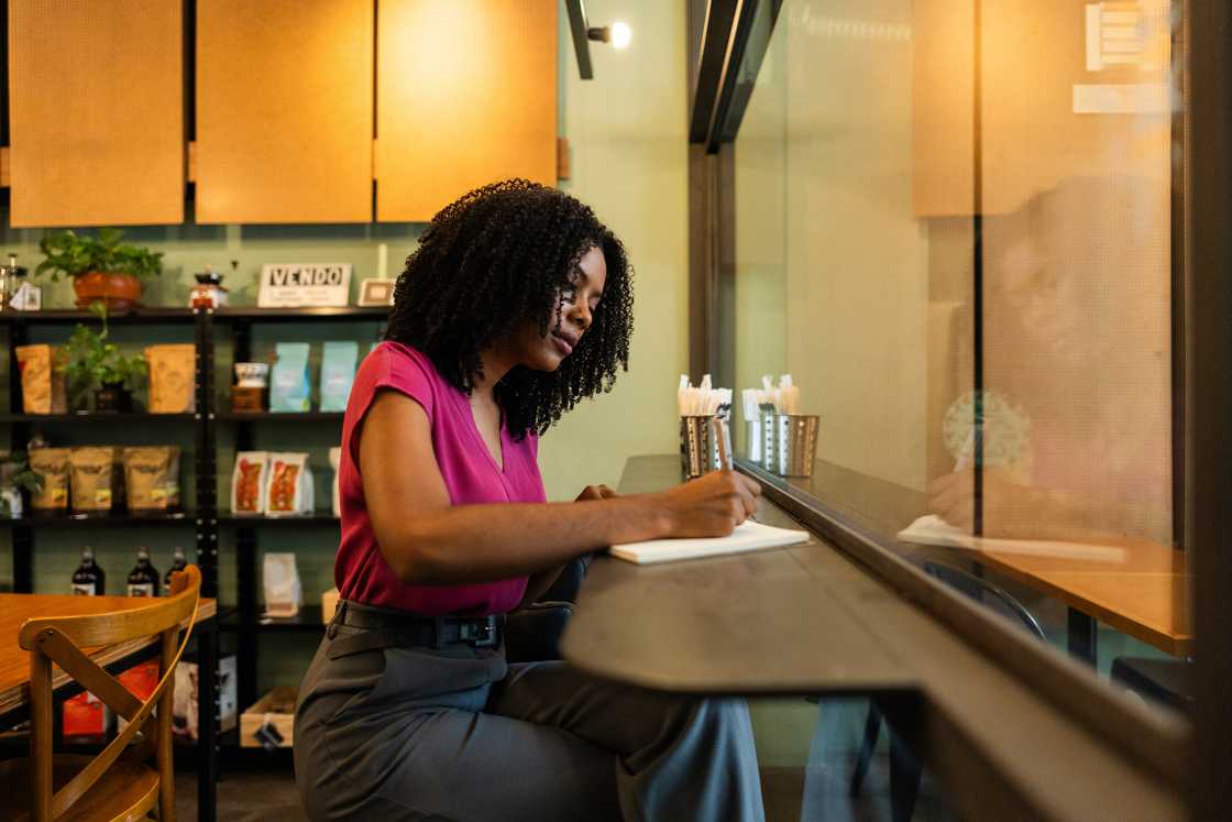 A woman writing in a notebook at a bagel shop table. A woman writing in a notebook at a bagel shop table.