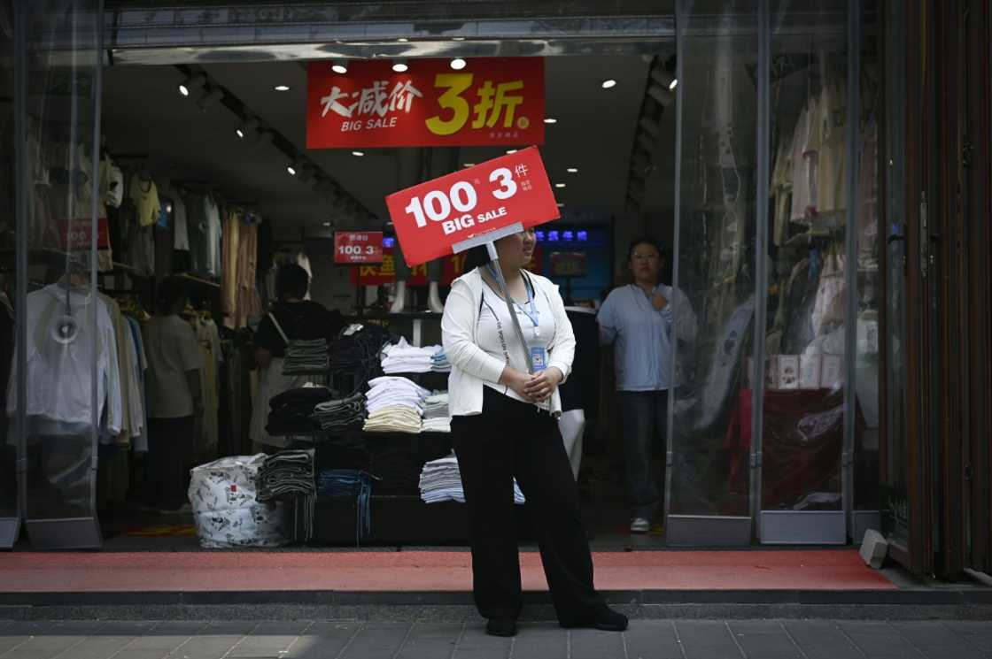 A staff member holds a board while waiting for customers at the entrance of a clothing store in Beijing A staff member holds a board while waiting for customers at the entrance of a clothing store in Beijing