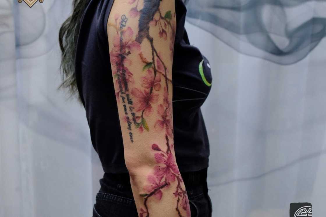 A woman in black is wearing a full sleeve cherry blossom tattoo