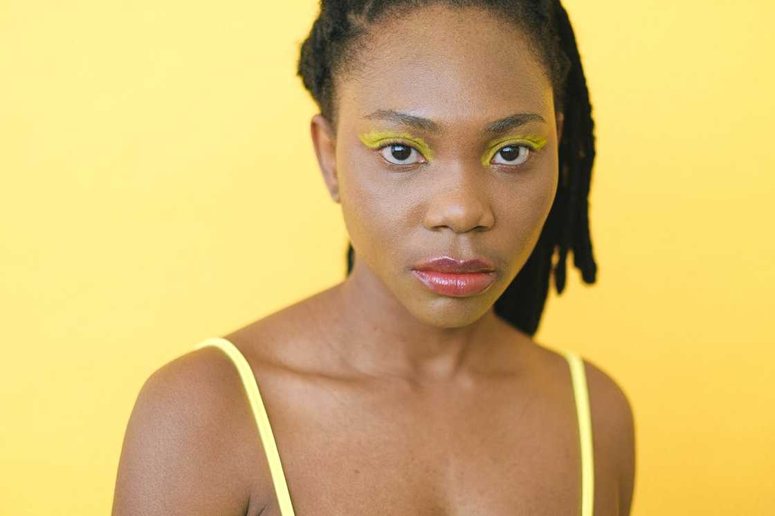 A woman with bold yellow makeup looks directly at the camera.