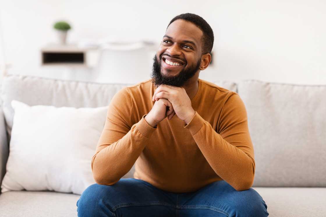 A man thinking and smiling while sitting on the couch at home.