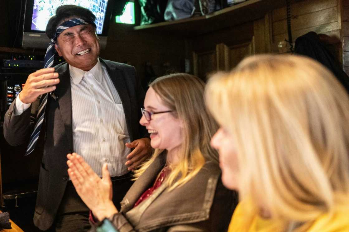 A Japanese man cracks jokes with tourists at a snack bar in Tokyo