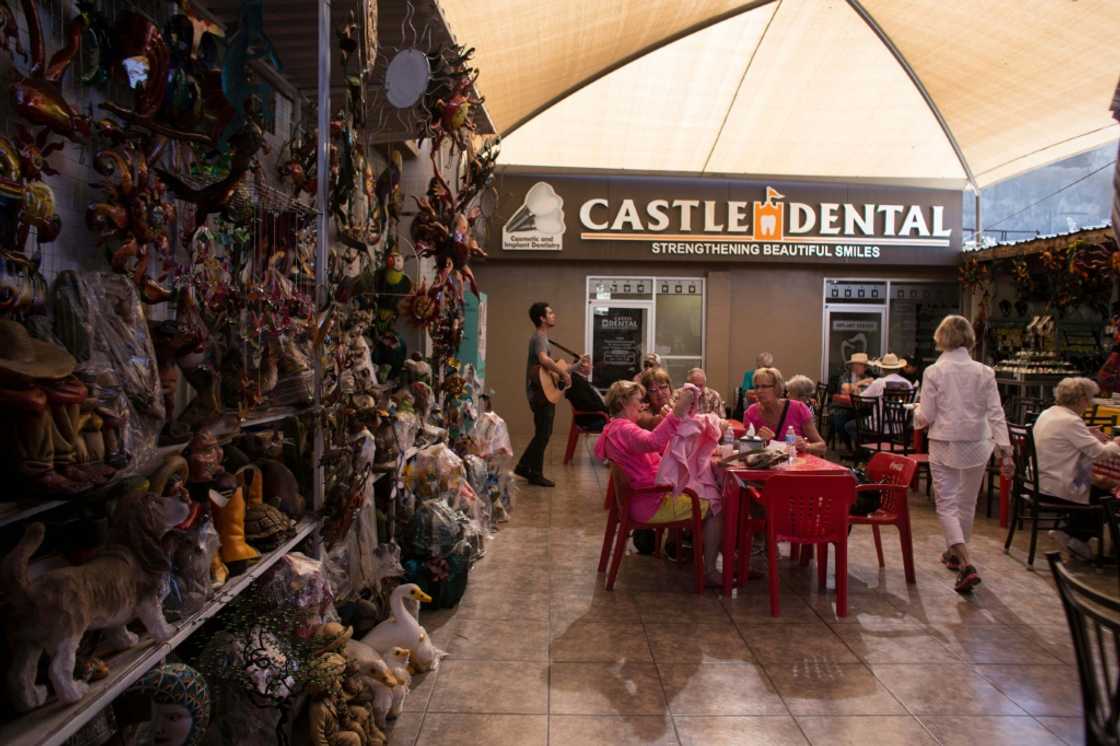 In this photo taken on February 15, 2017 visitors from the United States sit near a souvenir stand and dental clinic in downtown Los Algodones, near the US/Mexico border, northwestern Mexico In this photo taken on February 15, 2017 visitors from the United States sit near a souvenir stand and dental clinic in downtown Los Algodones, near the US/Mexico border, northwestern Mexico
