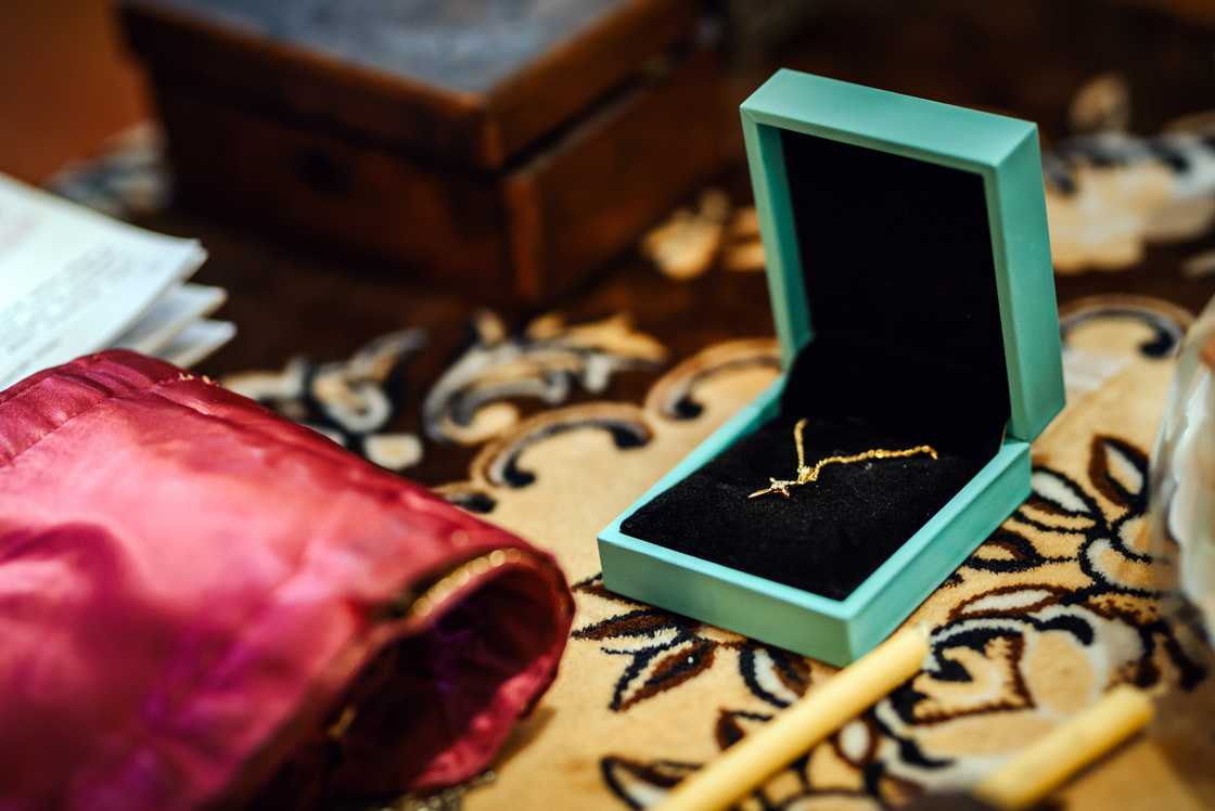 Open turquoise jewelry box with a gold cross necklace inside.