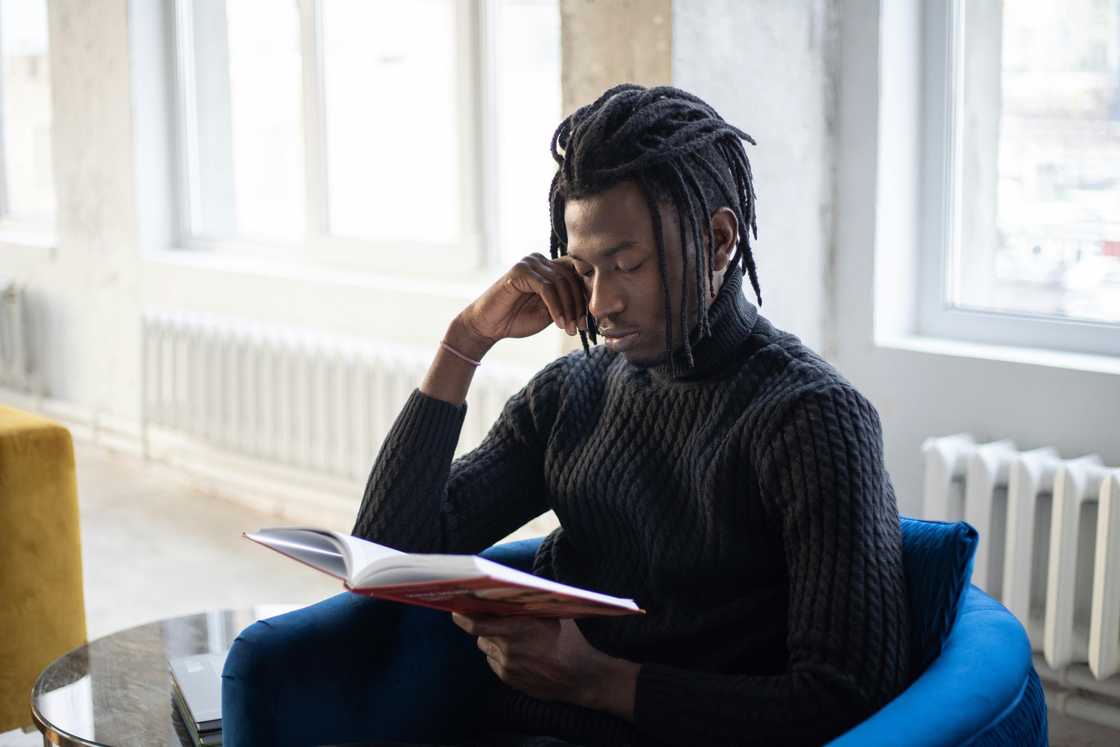 A young man in dreadlocks and a black sweater is reading a book A young man in dreadlocks and a black sweater is reading a book