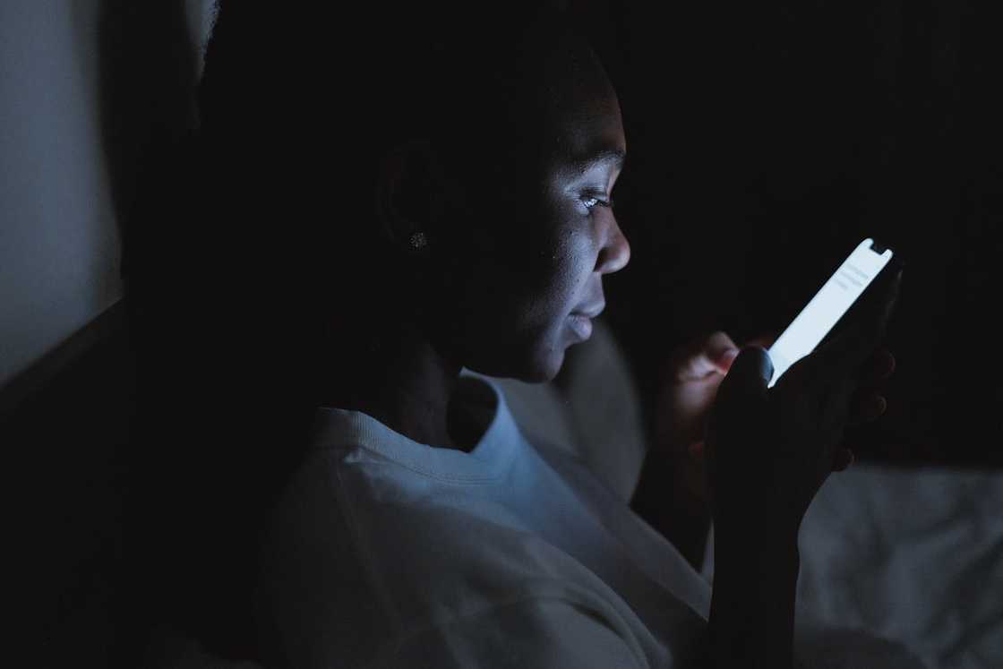 A woman sits in a dark room looking at her phone. A woman sits in a dark room looking at her phone.