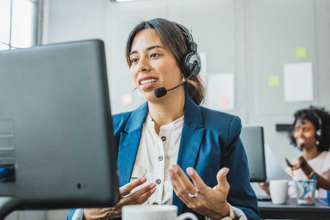 A friendly woman in call centre service is talking with customers through a headset.