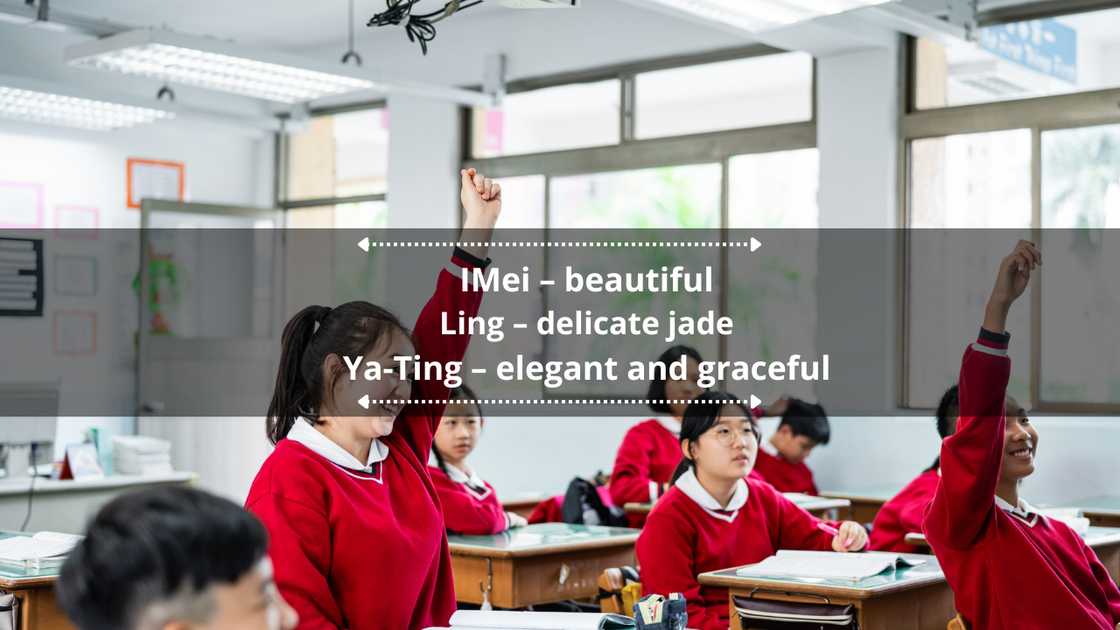 Cheerful schoolgirls with their hands raised, sitting with friends in the classroom.