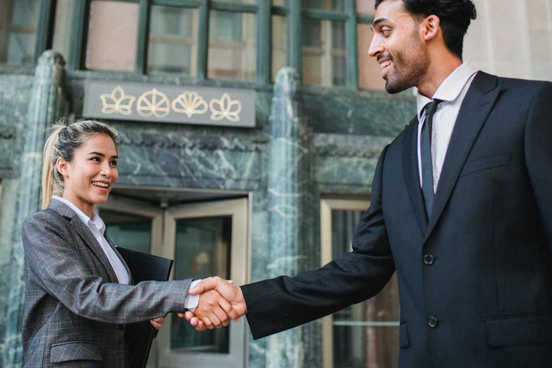 Two people smiling and shaking hands outside an office building. Two people smiling and shaking hands outside an office building.