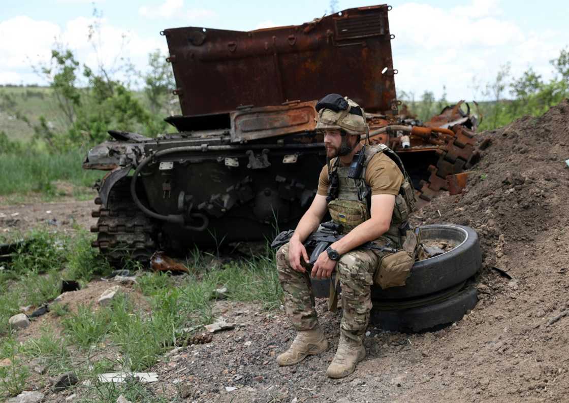 A Ukrainian serviceman sits next to a destroyed Russian tank not far from Lysychansk on Friday