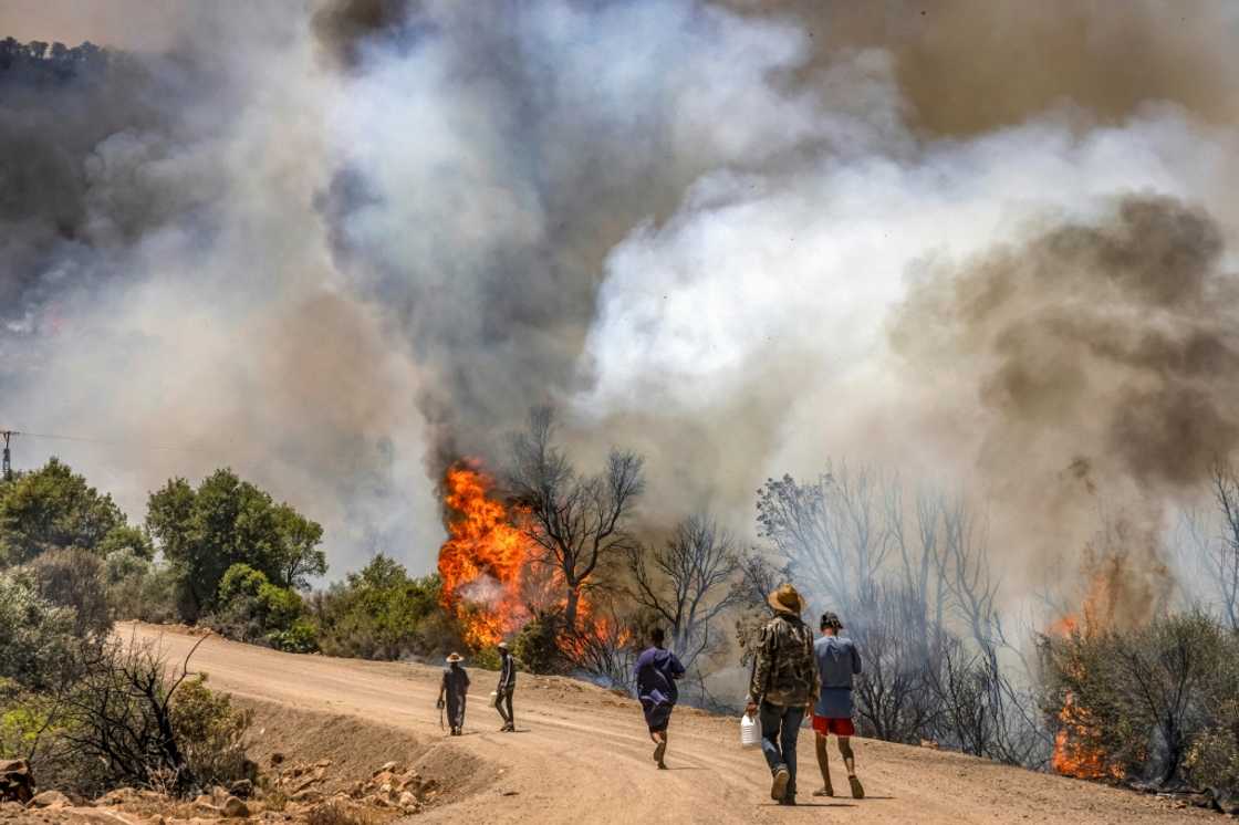 People walk along a dirt road as nearby a wild forest fire rages in Morocco's northern region of Ksar Sghir People walk along a dirt road as nearby a wild forest fire rages in Morocco's northern region of Ksar Sghir