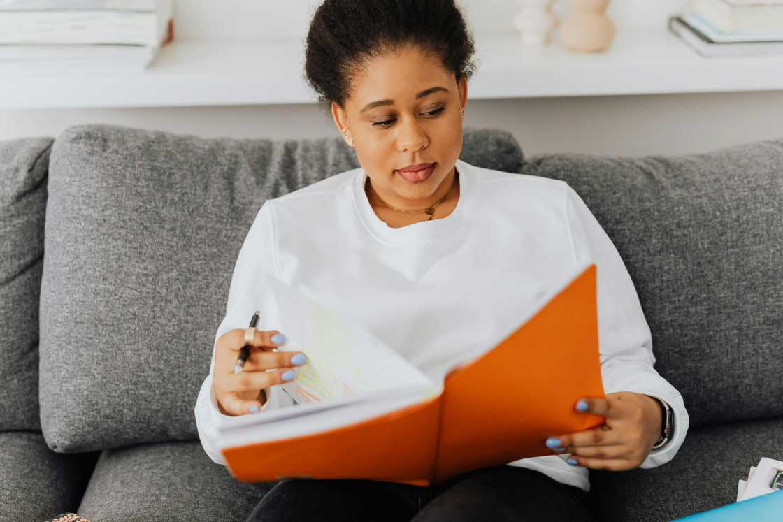 A young woman is reading a book with an orange cover A young woman is reading a book with an orange cover