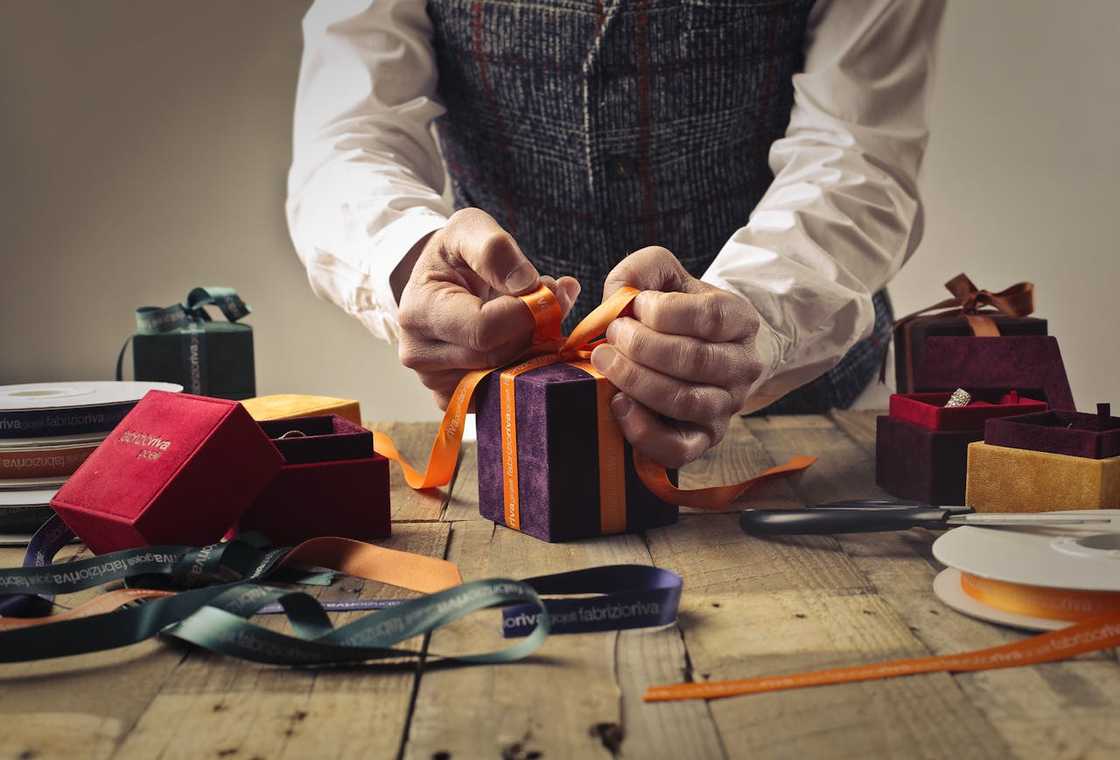 A person ties a ribbon on a purple gift box.