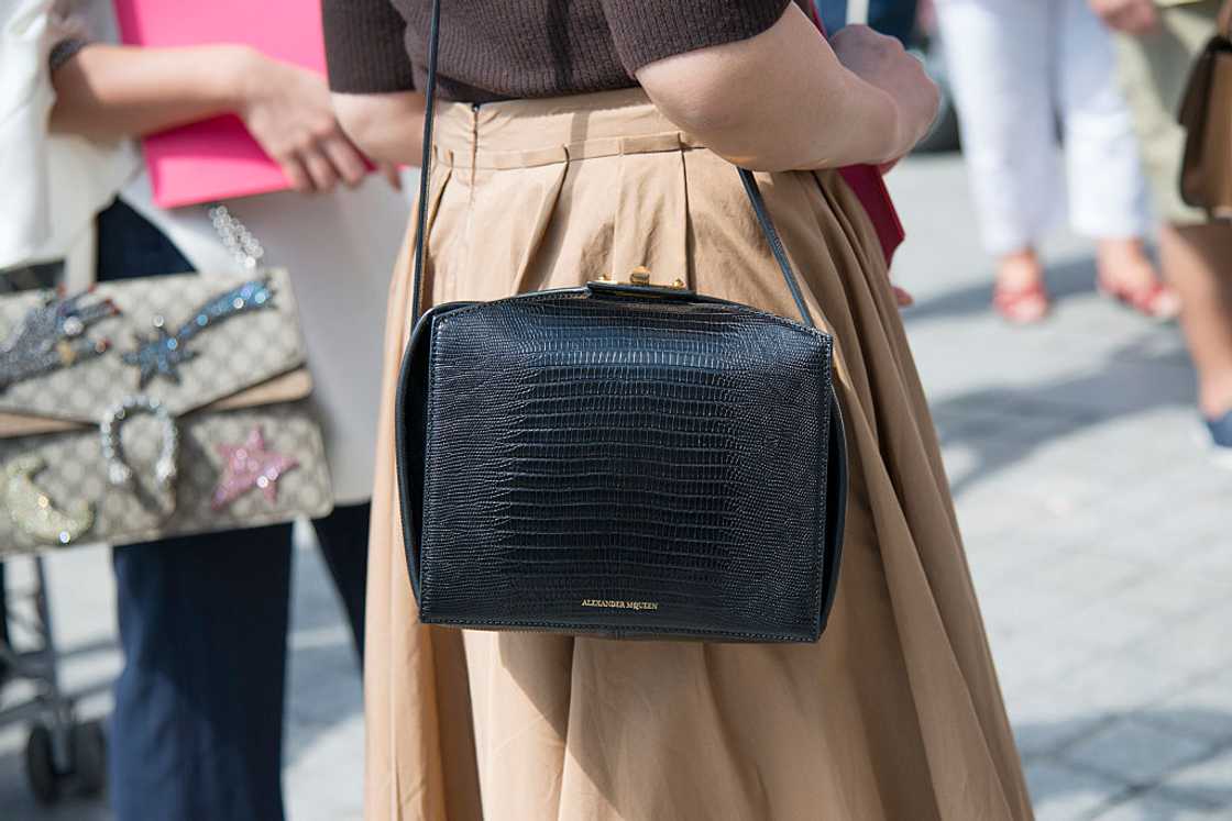 A woman stylishly carries an Alexander McQueen black purse on her shoulder. A woman stylishly carries an Alexander McQueen black purse on her shoulder.