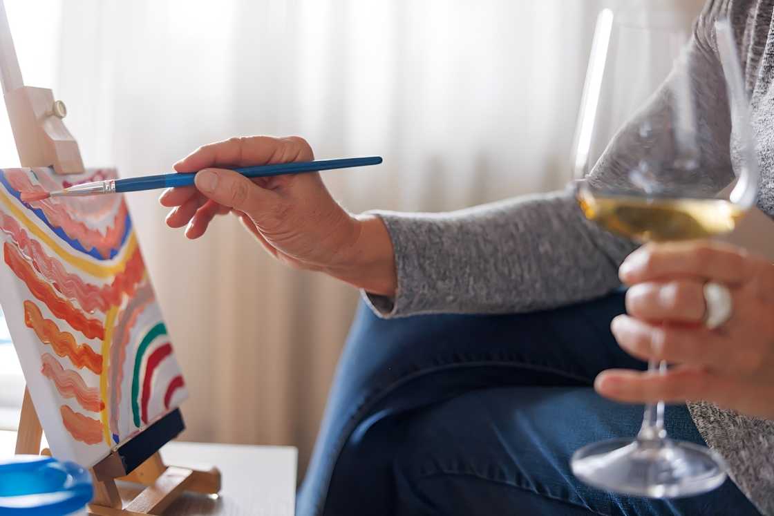 A senior Caucasian woman is drinking wine and painting A senior Caucasian woman is drinking wine and painting