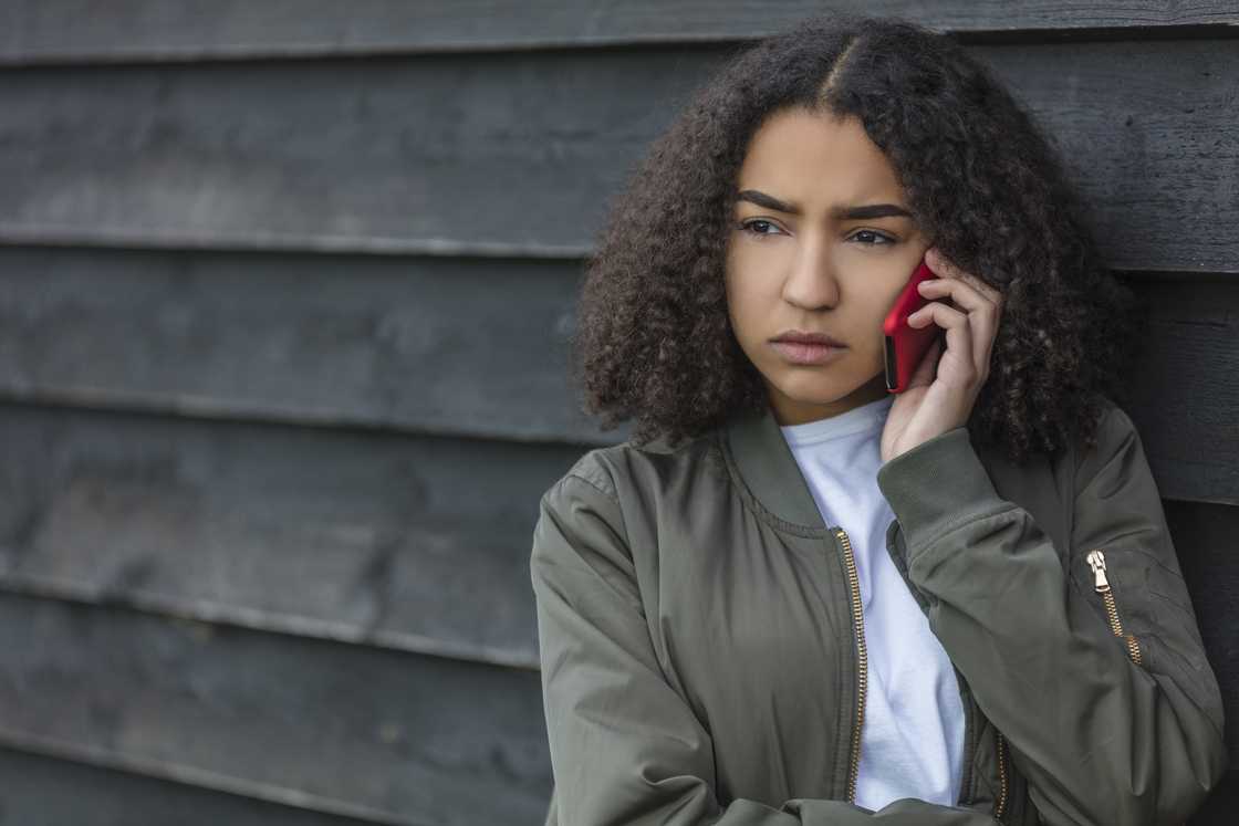 Person with curly hair holds a red phone to their ear. Person with curly hair holds a red phone to their ear.