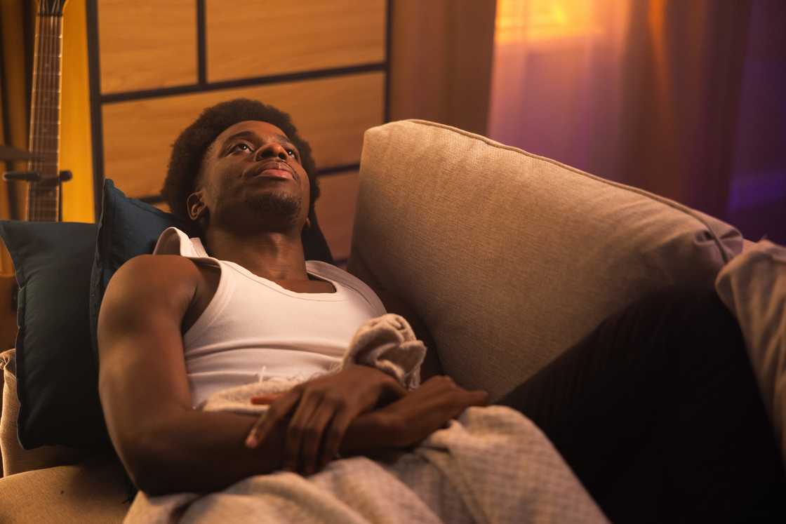 A person curled under blanket on friend’s sofa at night.