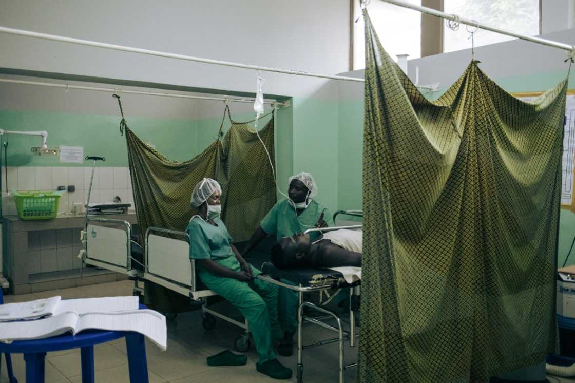 Two nurses sit beside a patient recovering from surgery