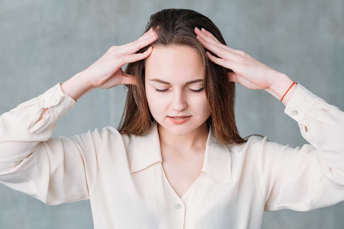 A young woman with closed eyes applies gentle, relaxing pressure on her head