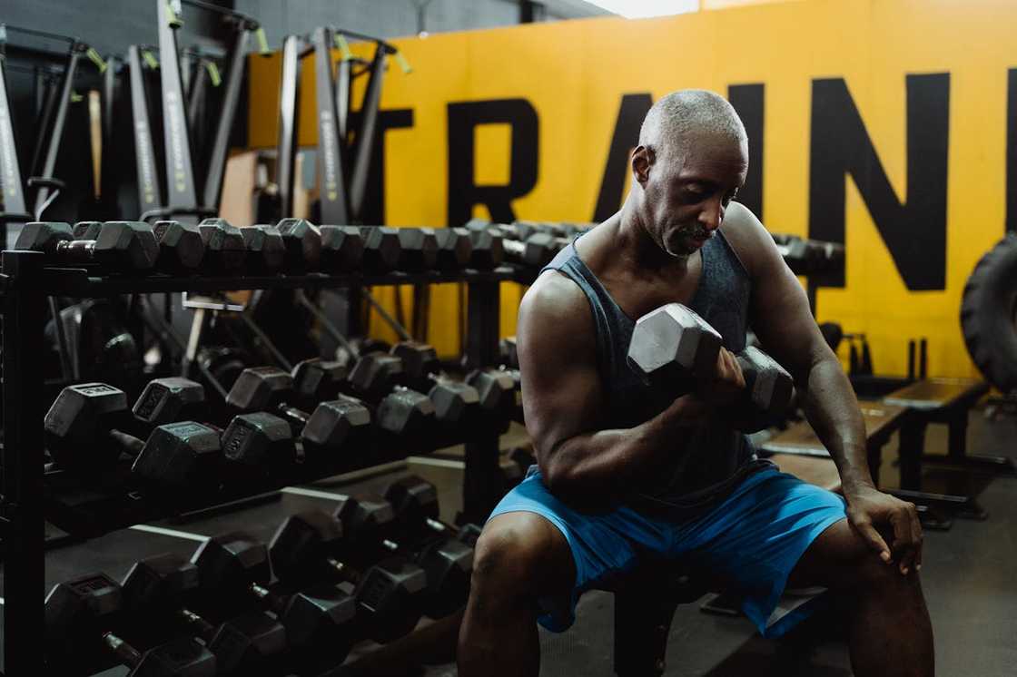 A man lifts a dumbbell while seated in a gym surrounded by weights. A man lifts a dumbbell while seated in a gym surrounded by weights.