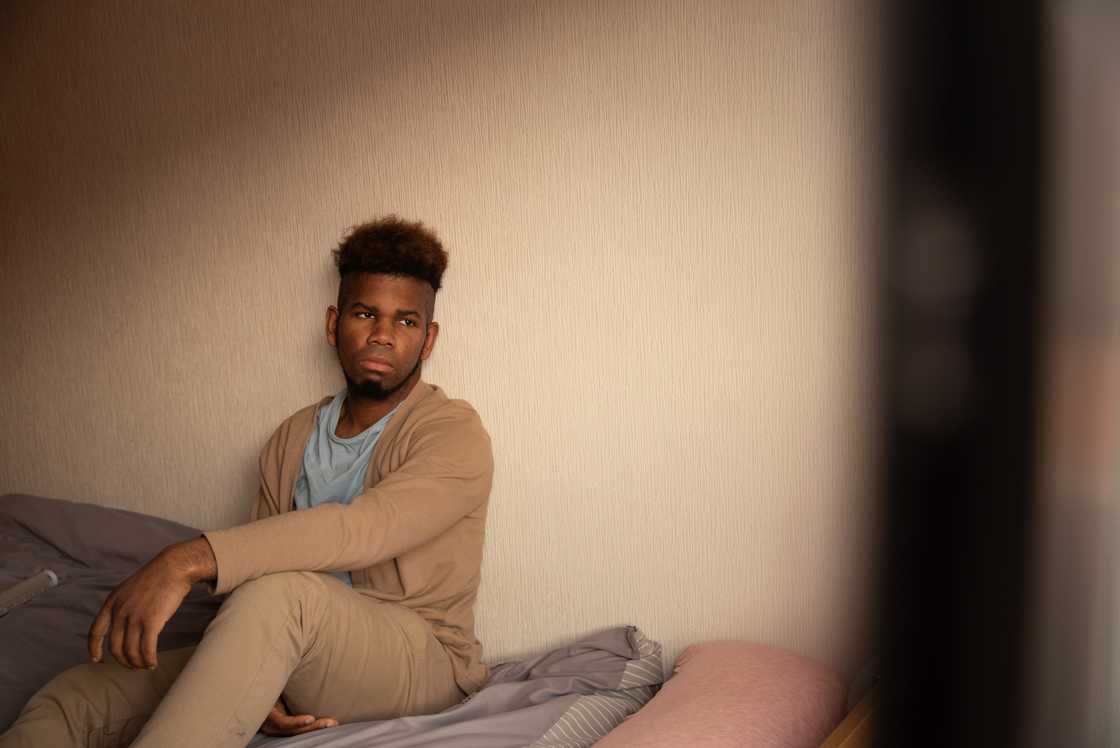 A young adult sitting alone on a bedroom floor.