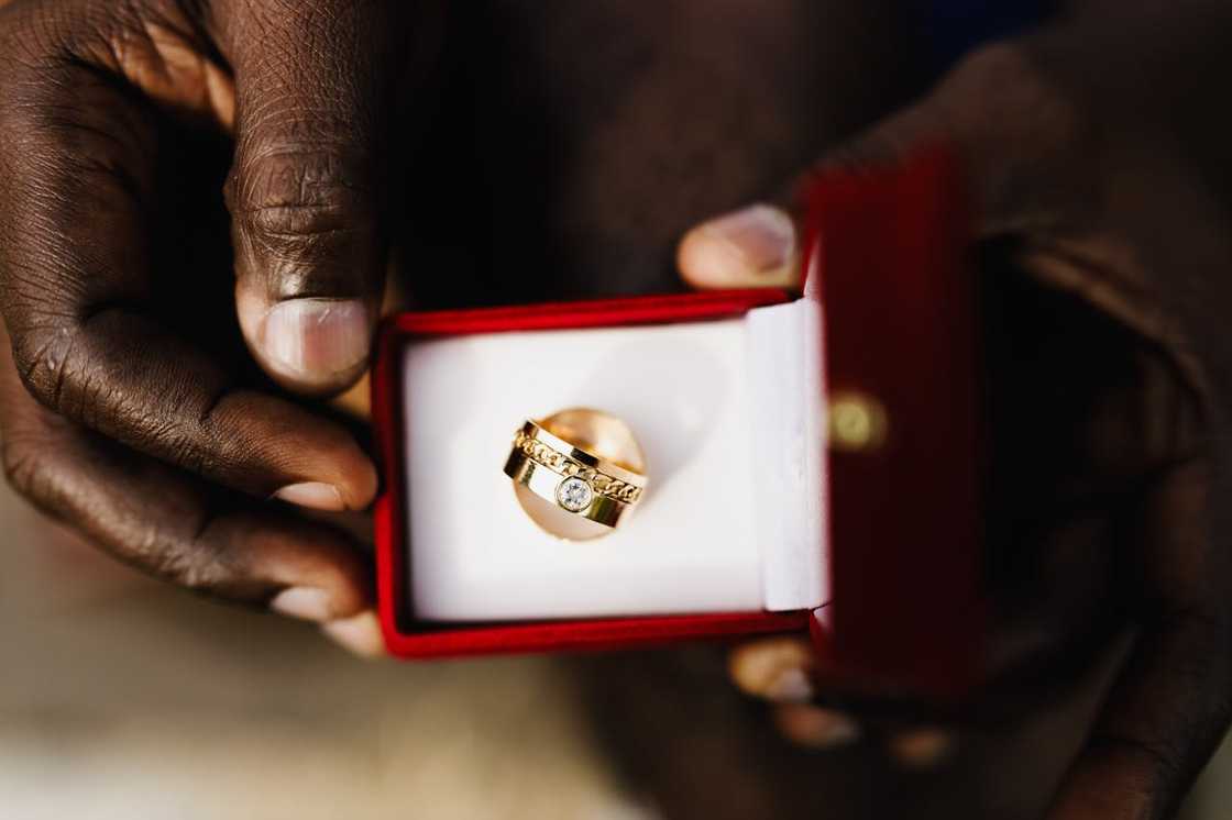 A person holds an open ring box displaying a gold ring. A person holds an open ring box displaying a gold ring.