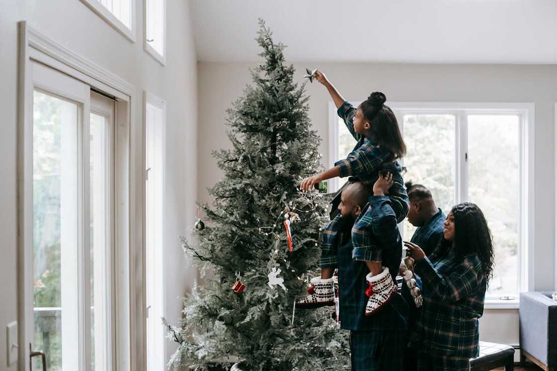 A girl places a Christmas star on a Christmas tree.