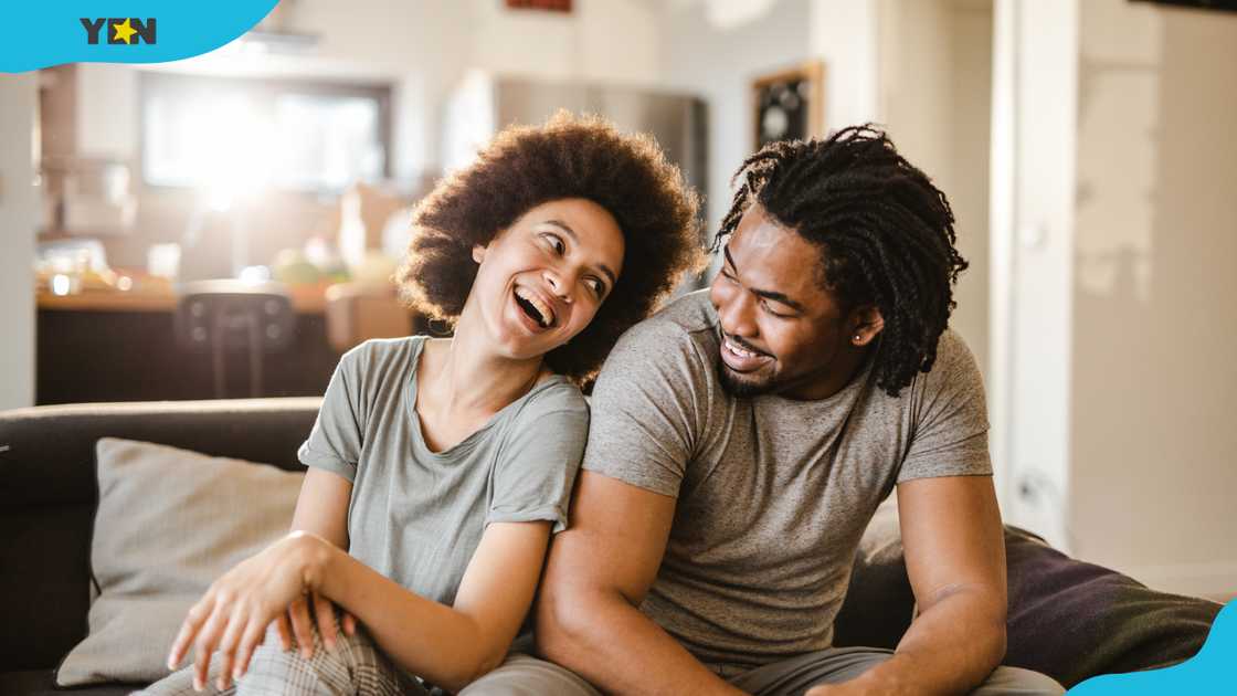 A cheerful black couple have fun while talking on the sofa at home.