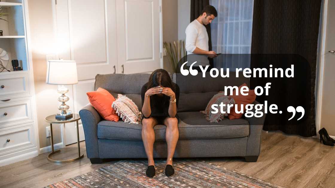 A woman sits on a sofa with her head in her hands while a man stands behind her checking his phone. A woman sits on a sofa with her head in her hands while a man stands behind her checking his phone.