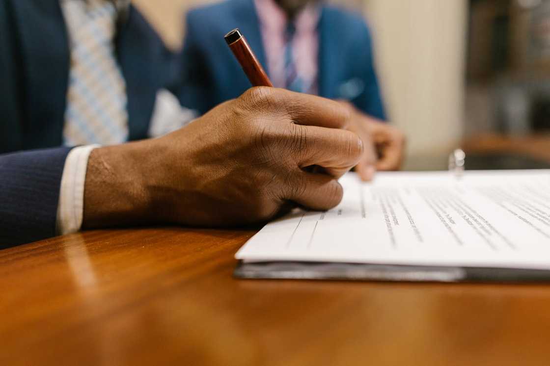 Close-up of a hand signing documents at a wooden desk.