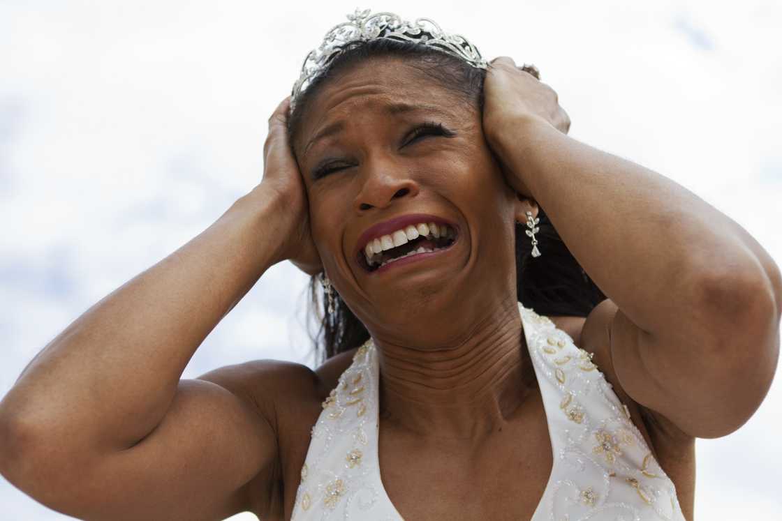 A bride in a tiara holding her head in distress.