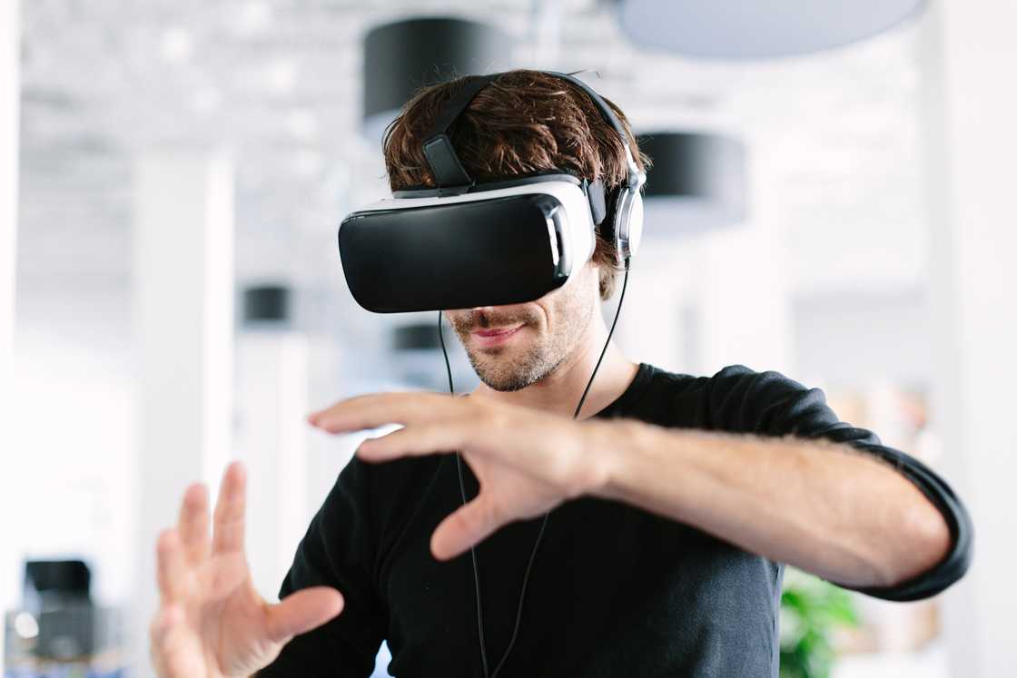 A young man wearing virtual reality glasses and gesturing in the office